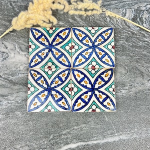 Puede incluir: Cuatro baldosas de cerámica cuadradas con un diseño floral. Cada baldosa presenta un patrón azul, turquesa, amarillo y blanco. Las baldosas están dispuestas en forma cuadrada, con un fondo neutro. Hay elementos decorativos en el fondo.