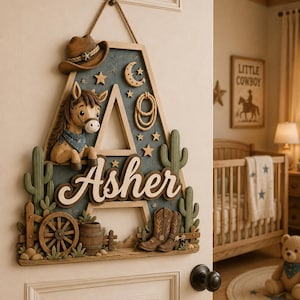 Puede incluir: Un letrero decorativo de madera con forma de letra A, que presenta un sombrero de vaquero marrón, un caballo, un lazo, estrellas, una luna creciente, cactus verdes, una rueda de carreta, un barril y botas de vaquero con el nombre Asher.