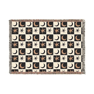 May include: Woven throw blanket with a repeating pattern of black and cream checkerboard squares. Each square features a gold crescent moon or star. The blanket has a fringed edge.