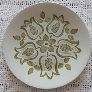 May include: A white ceramic plate with a green floral design. The design features stylised tulips with a central flower.