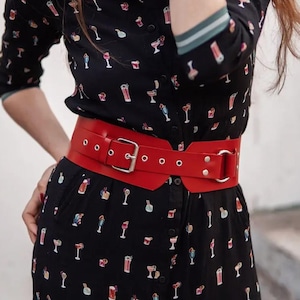 May include: A black button-down dress with a cocktail print, paired with a wide red belt. The belt has a silver buckle and multiple eyelets. The dress has long sleeves with a green and white striped trim.