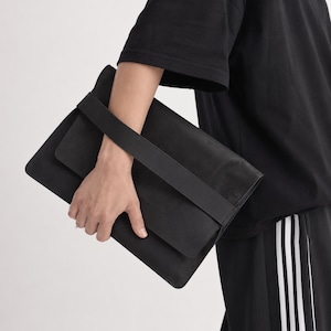 May include: A black leather messenger bag with a flap closure and a long shoulder strap. The bag is rectangular and appears to be made of a soft, matte leather. The strap is also black and appears to be made of the same material.