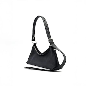 May include: Black shoulder bag with a crescent shape. The bag features a silver zipper, a long adjustable strap, and a silver metal ring. The bag is made of a smooth material.