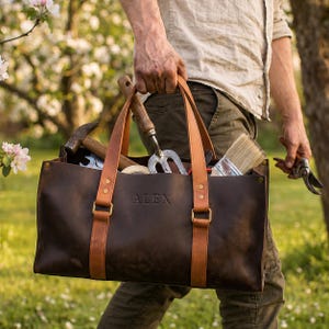 Personalized large leather tool bag held by man, custom engraved leather tool tote with garden and workshop tools