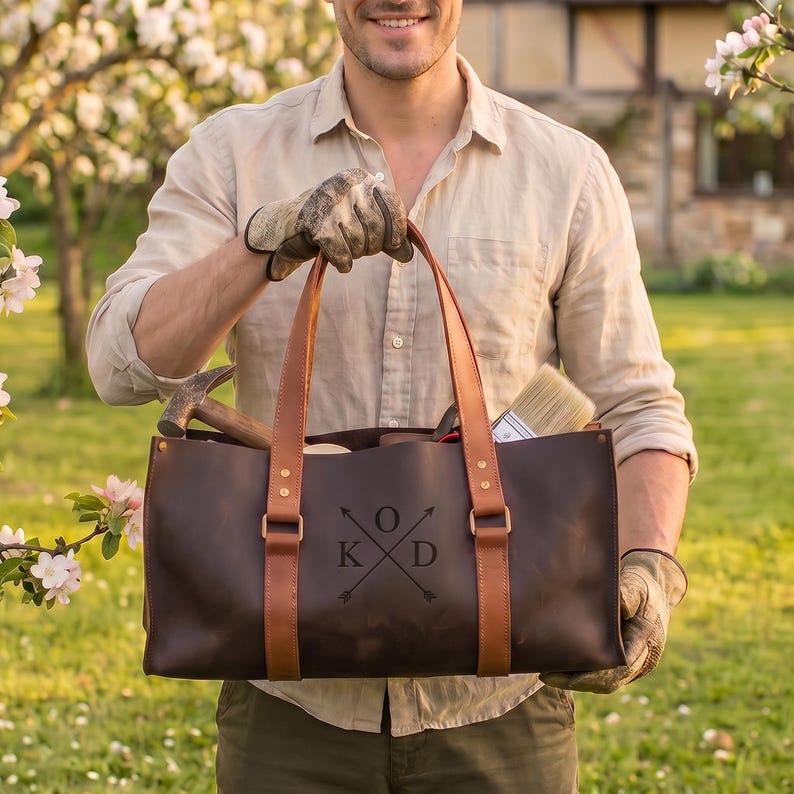 Personalized large leather tool bag held by man, custom engraved leather tool tote with garden and workshop tools