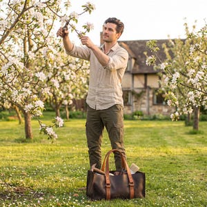 Man pruning trees in garden with large leather tool bag nearby, practical gardening tote and outdoor tool organizer