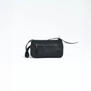 K&ouml;nnte beinhalten: Eine schwarze, rechteckige Umh&auml;ngetasche mit Rei&szlig;verschluss und einem langen, d&uuml;nnen Riemen. Die Tasche hat eine kleine, rechteckige Tasche auf der Vorderseite und einen silbernen Rei&szlig;verschluss. Die Tasche ist aus mattem Material.