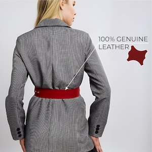 May include: A grey and white houndstooth blazer with a wide red leather belt. The belt has a simple buckle closure. The text "100% GENUINE LEATHER" is visible in the image.