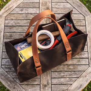 Large dark brown leather tool bag with cognac handles on wooden garden table, handmade garden tool tote for DIY and garage tools