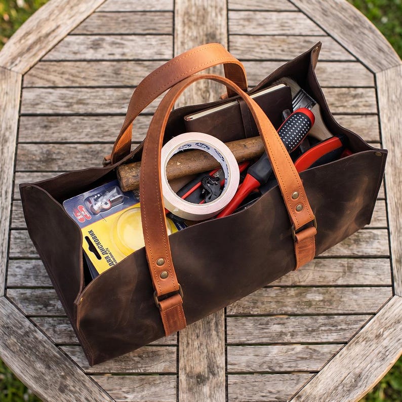 Large dark brown leather tool bag with cognac handles on wooden garden table, handmade garden tool tote for DIY and garage tools