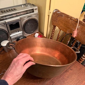 Peut inclure: Un grand bassin en cuivre antique avec deux poignées latérales, posé sur une table en bois. Le bassin a une forme ovale large et une couleur brun-rougeâtre chaude. Un vieux boombox est visible en arrière-plan.