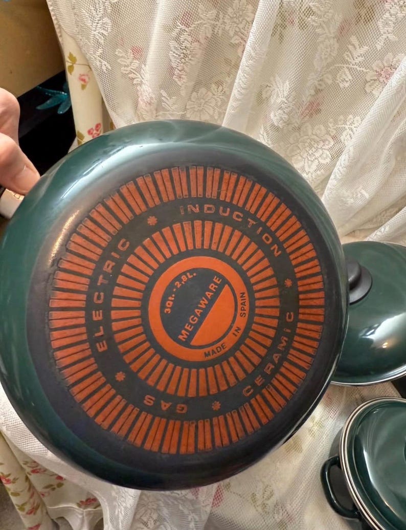 May include: A set of green ceramic cookware with orange and black detailing. The base of the pan features the text "ELECTRIC", "INDUCTION", "GAS", "MEGAWARE", and "MADE IN SPAIN". The pan has a capacity of 2.8 liters.
