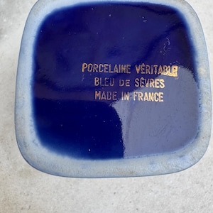 Puede incluir: Primer plano de un objeto cuadrado de porcelana azul cobalto con esquinas redondeadas. El texto dorado dice "PORCELAINE V&Eacute;RITABLE BLEU DE S&Egrave;VRES MADE IN FRANCE". El objeto tiene un borde azul claro.