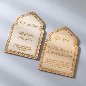 May include: Two wooden plaques with Islamic prayers for Suhoor and Iftar. The plaques have an arched top and intricate border designs. The text is in Arabic and English, with the English translation below. The wood has a light brown colour.
