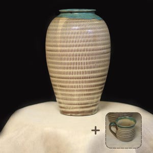 Puede incluir: Un jarrón de cerámica hecho a mano con un patrón de rayas verticales texturizadas en crema y marrón. El jarrón tiene un borde turquesa y está sobre una superficie blanca. También se muestra una taza a juego con un asa.