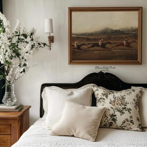 K&ouml;nnte beinhalten: Ein Schlafzimmer mit einem gerahmten Vintage-Druck eines Pferderennens &uuml;ber einem Bett mit wei&szlig;en und floralen Kissen. Ein Nachttisch aus Holz h&auml;lt eine Vase mit wei&szlig;en Blumen. Der Text "Bloom Ridge Prints" ist sichtbar.