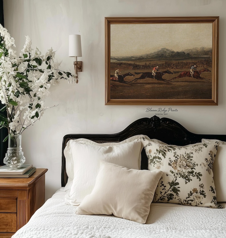K&ouml;nnte beinhalten: Ein Schlafzimmer mit einem gerahmten Vintage-Druck eines Pferderennens &uuml;ber einem Bett mit wei&szlig;en und floralen Kissen. Ein Nachttisch aus Holz h&auml;lt eine Vase mit wei&szlig;en Blumen. Der Text "Bloom Ridge Prints" ist sichtbar.