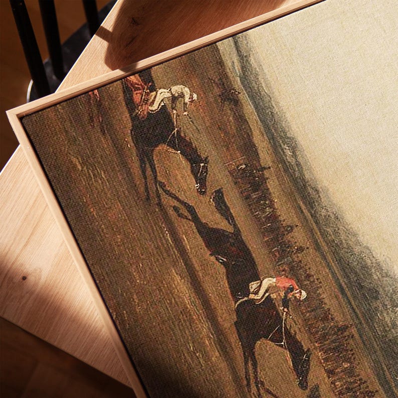 K&ouml;nnte beinhalten: Gerahmter Leinwanddruck einer Pferderennszene. Das Kunstwerk zeigt zwei Jockeys auf Pferden, die &uuml;ber ein braunes und gr&uuml;nes Feld rennen. Die Pferde werfen lange Schatten. Der Rahmen ist aus hellem Holz gefertigt.