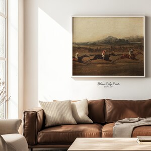 K&ouml;nnte beinhalten: Ein gerahmter Vintage-Druck, der ein Pferderennen mit drei Jockeys zeigt. Das Kunstwerk in ged&auml;mpften T&ouml;nen h&auml;ngt &uuml;ber einem braunen Ledersofa. Der Text "Bloom Ridge Prints DIGITAL ART" ist sichtbar. Die Szene erweckt einen historischen Eindruck.