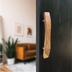 May include: A wooden door handle with a natural, organic shape. The handle is made of light and dark brown wood, attached to a black door with silver hardware. The design is modern and rustic, suitable for interior decor.