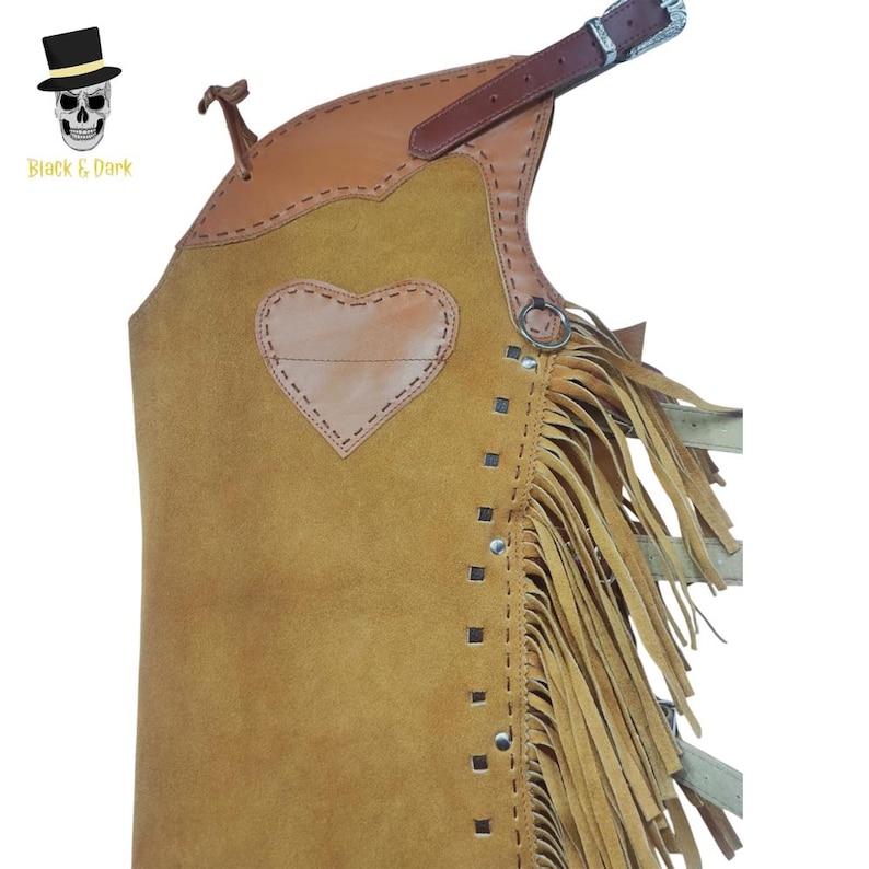 May include: A tan leather chaps with a brown leather top and a heart-shaped patch. The chaps have fringe along the side and a silver buckle. The text "Black & Dark" is in the upper left corner.
