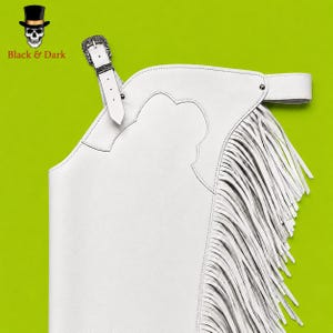 May include: A white leather chaps garment featuring long fringe detailing along the side, a decorative silver-toned metal buckle closure at the top, and a wide adjustable waist strap. The design includes stitched paneling and a smooth finish.