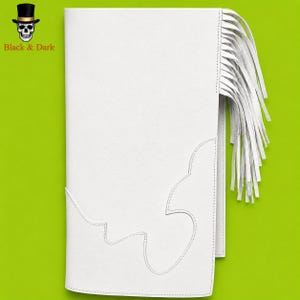 May include: A white rectangular leather-like accessory featuring a long fringe detail on the right side and decorative stitching along the bottom edge. The top left corner displays a small black top hat and skull logo with the text Black & Dark.