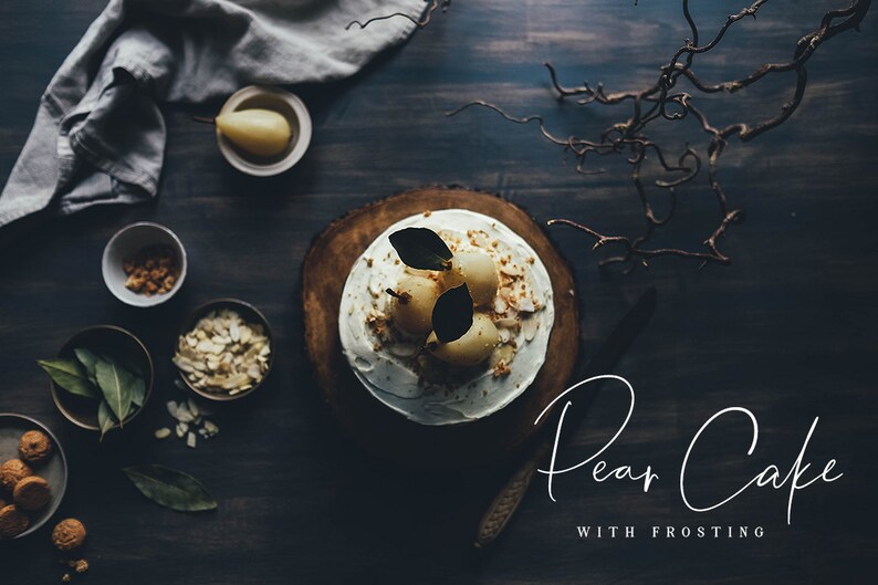 Puede incluir: Un pastel de pera blanco con glaseado y peras en rodajas en la parte superior, decorado con almendras. El pastel est&aacute; sobre una tabla de madera y el fondo es una superficie de madera oscura.
