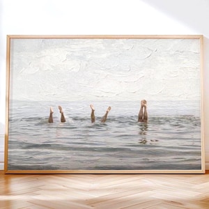 Puede incluir: Una impresión de arte mural enmarcada que presenta una representación texturizada y pictórica de tres pares de piernas que se extienden verticalmente fuera de un agua oceánica gris y tranquila bajo un cielo nublado. Marco de madera clara.
