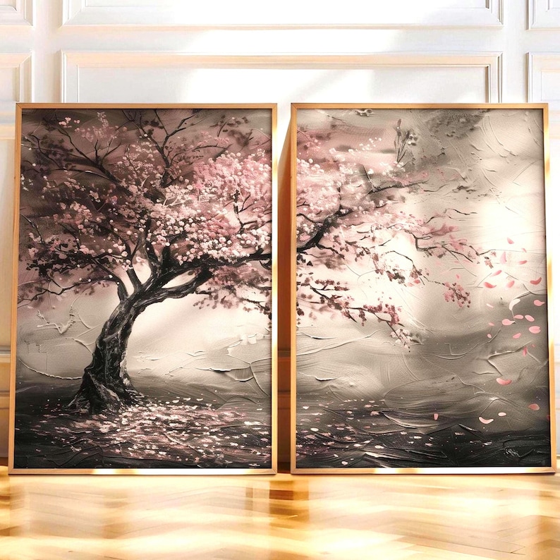 two framed paintings of a tree with pink flowers, displayed on a wooden floor against a white wall.