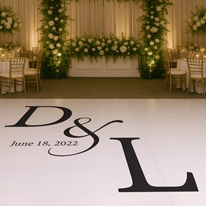 Puede incluir: Una pista de baile blanca con letras negras que dicen "D & L" y "18 de junio de 2022". El fondo presenta un escenario de recepción de boda con arreglos florales y mesas.