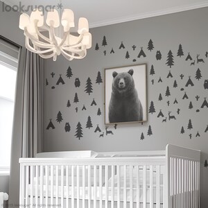 Puede incluir: Una habitación de bebé con una cuna blanca y una pared gris con calcomanías negras de animales del bosque y árboles. Una foto en blanco y negro de un oso cuelga de la pared. La habitación tiene una lámpara de araña blanca con un diseño único.