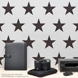 May include: A white wall with a black star pattern. A black camera, a black folder, and a black box are on a wooden surface in front of the wall.