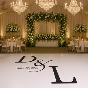 Puede incluir: Un lugar de recepci&oacute;n de bodas con una pista de baile blanca con las iniciales "D & L" y la fecha "18 de junio de 2022". La sala est&aacute; decorada con arreglos florales, candelabros y mesas preparadas para los invitados.