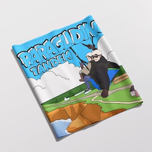 Könnte beinhalten: Ein blau-weißes Halstuch mit der Aufschrift "PARAGLIDING TANDEM". Die Grafik zeigt zwei Personen beim Tandem-Paragliding über einer Küstenlandschaft mit Klippen, Häusern und Wolken. Das Design ist eine Cartoon-Illustration.