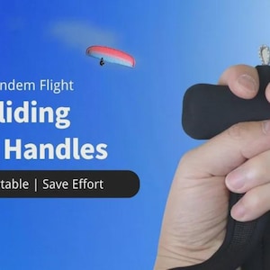 May include: Black paragliding brake handles with the text "Trick and Tandem Flight Paragliding Brake Handles". The handles are held in a hand against a blue sky background with a paraglider in the distance. The text also says "Comfortable | Save Effort".