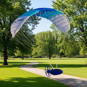 May include: A powered paraglider with a blue and white canopy is suspended in the air. The canopy has the word "KING" printed on it. The paraglider is over a green grassy area with a paved path.