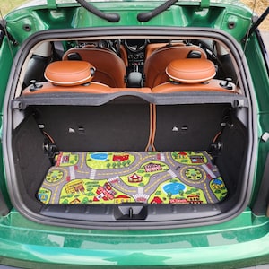 May include: A green hatchback car with the trunk open, revealing a colorful road map play mat. The interior features brown leather seats and a black storage area. The car's exterior is a vibrant green.