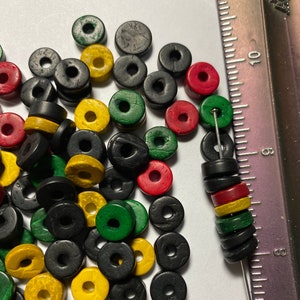 May include: A pile of wooden beads in black, red, yellow, and green colors. The beads are round with a hole in the center. They are arranged in a random pattern.