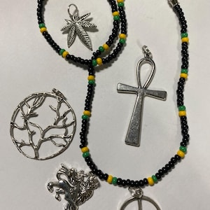 Peut inclure: Un collier de perles noires avec des accents verts et jaunes. Le collier a cinq breloques en argent : un signe de paix, un lion, un arbre, un ankh et une feuille de marijuana.