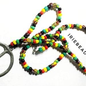 Può includere: Una collana con un ciondolo a forma di segno della pace e una catena di perline multicolori. Le perline sono nere, verdi, gialle e rosse. La catena è a strati e il ciondolo è argentato.