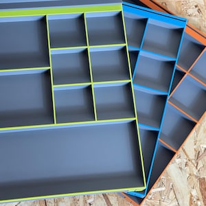 May include: Three rectangular drawer organizers with grey interiors and vibrant rims in lime green, bright blue, and orange. Each organizer features a grid of internal dividers creating multiple compartments of varying sizes for storage and organization.