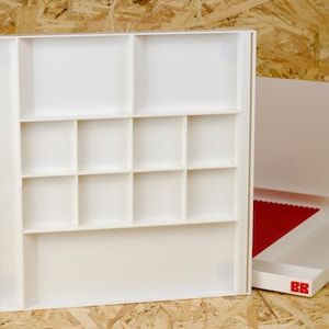 May include: White storage box with multiple compartments, ideal for organizing small items. The box is open, revealing a grid of square spaces. A second box with a red base is partially visible. The boxes have the letters "BB" in red.