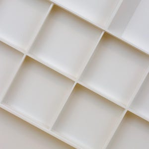 May include: A white, rectangular paint palette with multiple square and rectangular compartments. The palette is made of a smooth, matte material and is designed for mixing paints. The compartments are empty, ready for use.