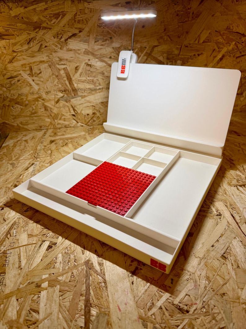 Puede incluir: Un organizador blanco con m&uacute;ltiples compartimentos y una placa base Lego roja. Cuenta con una luz LED y un panel trasero con bisagras. Dise&ntilde;ado para almacenar y organizar objetos peque&ntilde;os, ideal para pasatiempos.