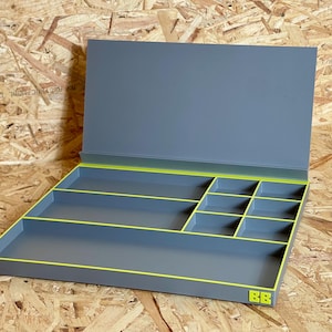 May include: A gray storage tray with a hinged lid and multiple interior compartments. The tray features bright lime green trim along the edges and a small lime green BB logo on the front corner. The interior is divided into various rectangular sections.