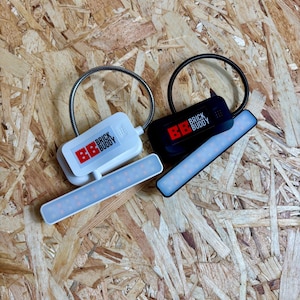 Puede incluir: Dos luces LED "Brick Buddy", una blanca y otra negra, con fijaciones de cuello de cisne de metal flexible. Cada luz tiene una base rectangular con el logotipo "Brick Buddy" en rojo y blanco. Las luces est&aacute;n sobre una superficie de vetas de madera.