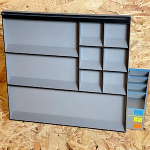 May include: A large rectangular gray organizer tray with black edges featuring two wide horizontal compartments and six smaller square compartments, accompanied by a separate vertical gray storage unit with blue, yellow, and orange accents.
