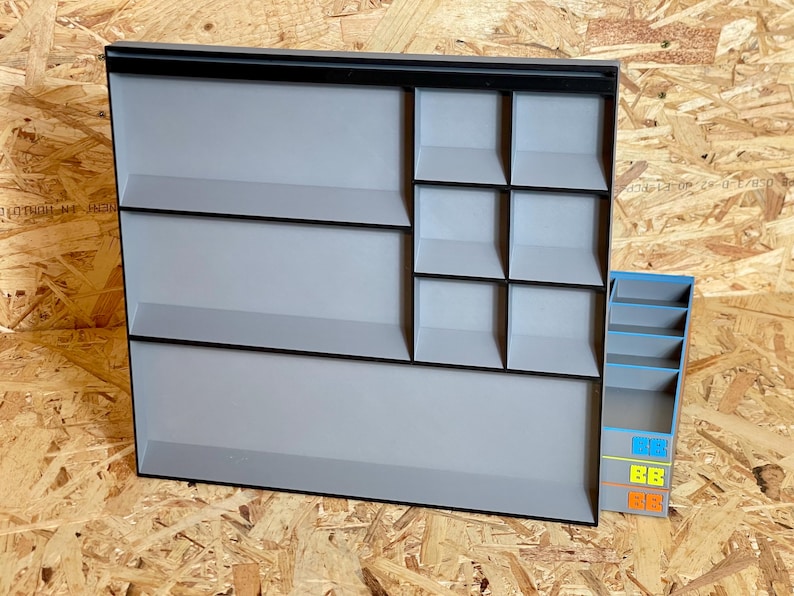 May include: A large rectangular gray organizer tray with black edges featuring two wide horizontal compartments and six smaller square compartments, accompanied by a separate vertical gray storage unit with blue, yellow, and orange accents.
