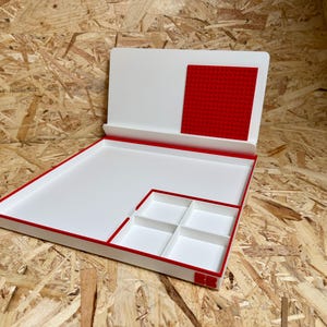 May include: A white and red organizer with a large tray, a small compartment with four sections, and a red square. The organizer has a red border and is open, revealing the interior.